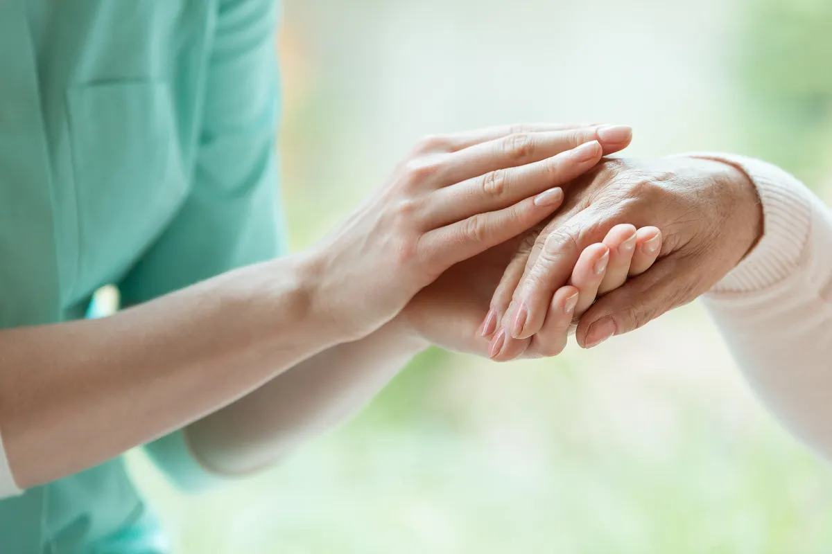 Custodia24 – 24-Stunden-Betreuungskräfte – Eine jüngere Hand hält und tröstet sanft die Hand einer älteren in einer liebevollen Geste.